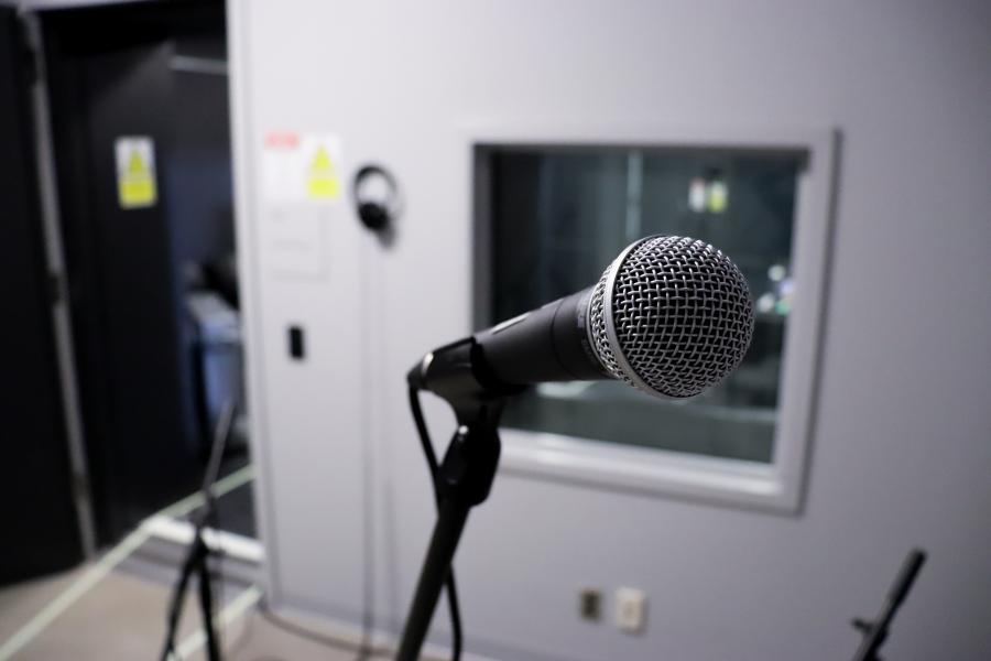 A microphone on a stand inside the School of Art’s audio recording booth, with the control room visible through the window.