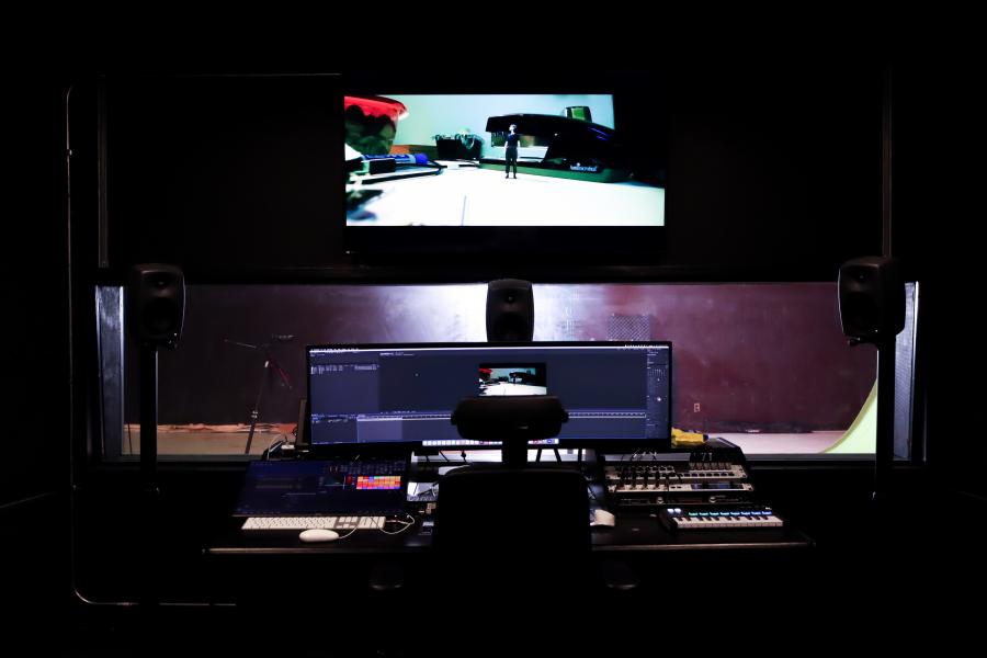 The Sound Stage control room setup with speakers, an editing station, and a large window looking into the studio’s green screen area.