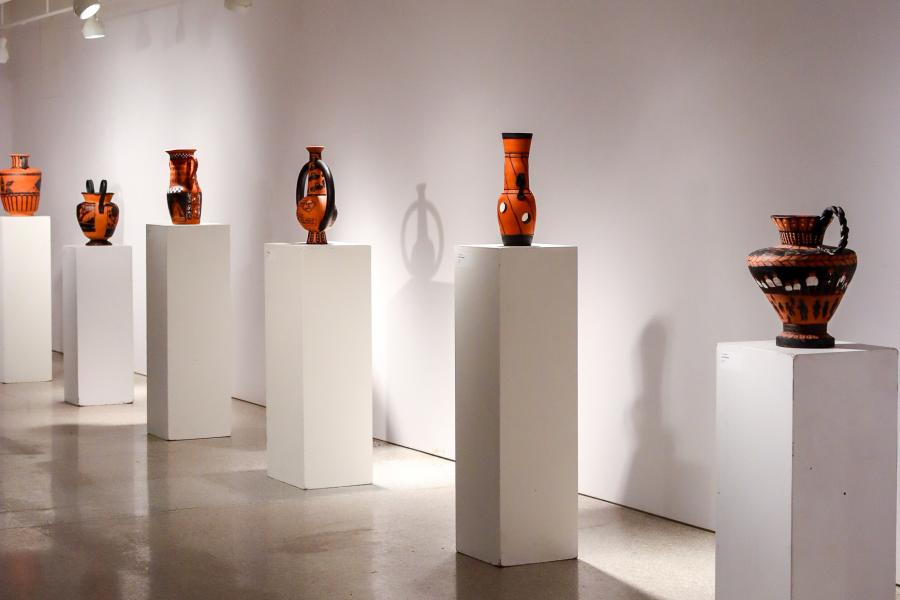 Row of ceramic vessels displayed on white pedestals in the gallery space.