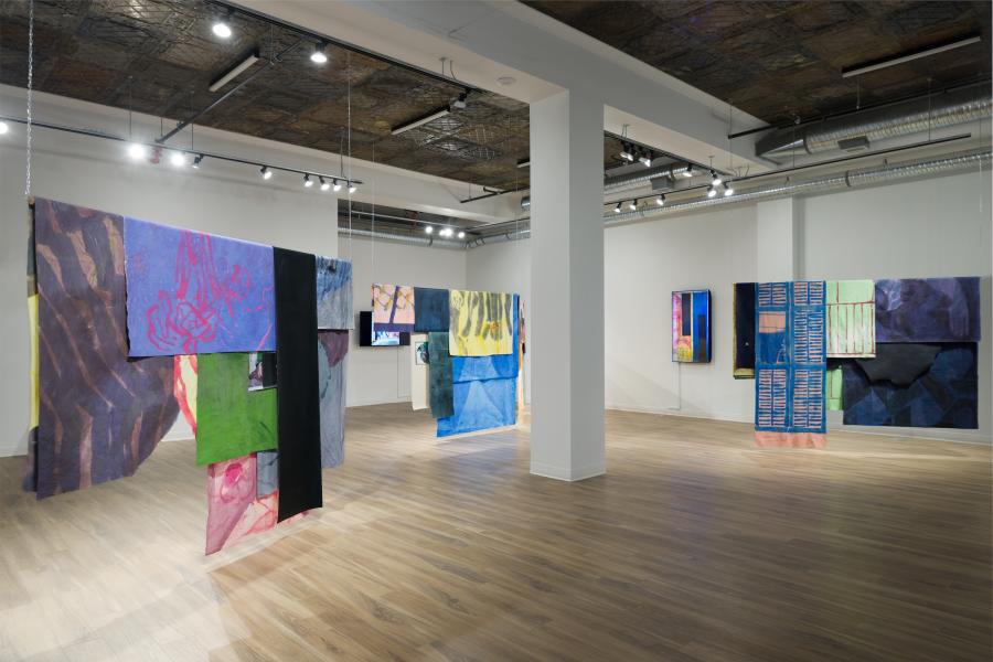 Installation view of suspended textile works arranged throughout a gallery, creating a layered, walk-through environment.