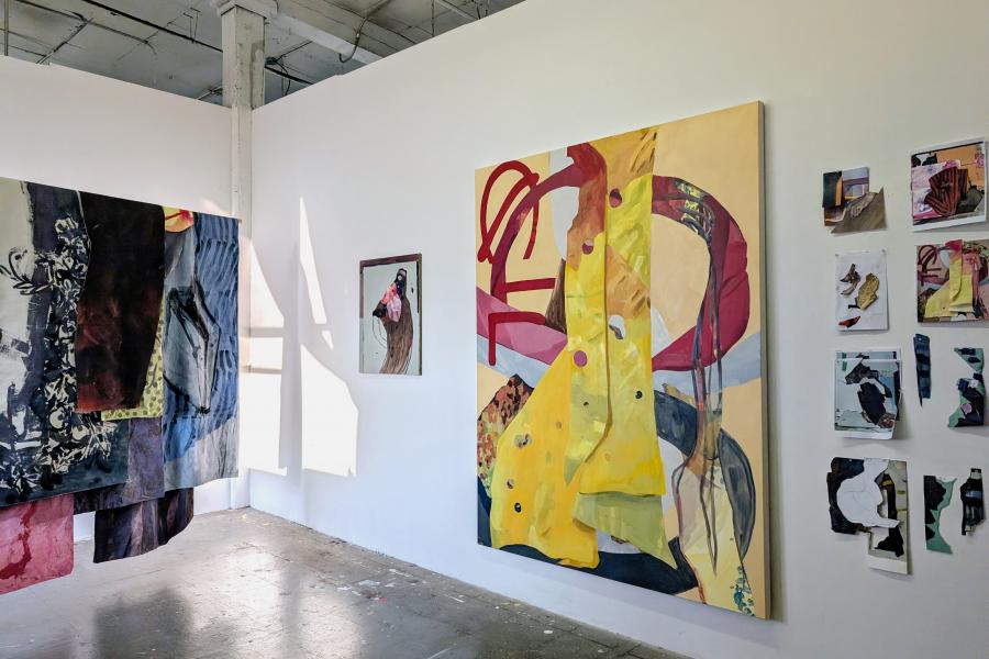 Studio installation view with layered textile and painted works arranged alongside pinned studies and works-in-progress on the wall.