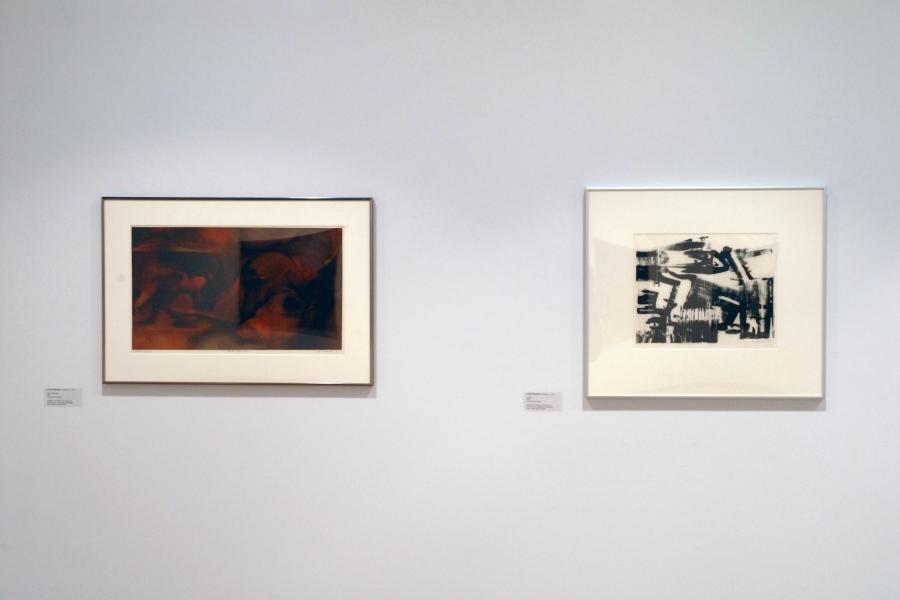 Two abstract graphics on a wall. The left one comprises red forms and a black rectangle underneath them, which is less clearly defined on the left than the right. The right one comprises black strokes on a white background.