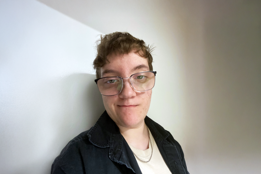 Instructor portrait of Jasmin Reimer wearing glasses and a dark jacket, standing against a light wall with soft natural light.