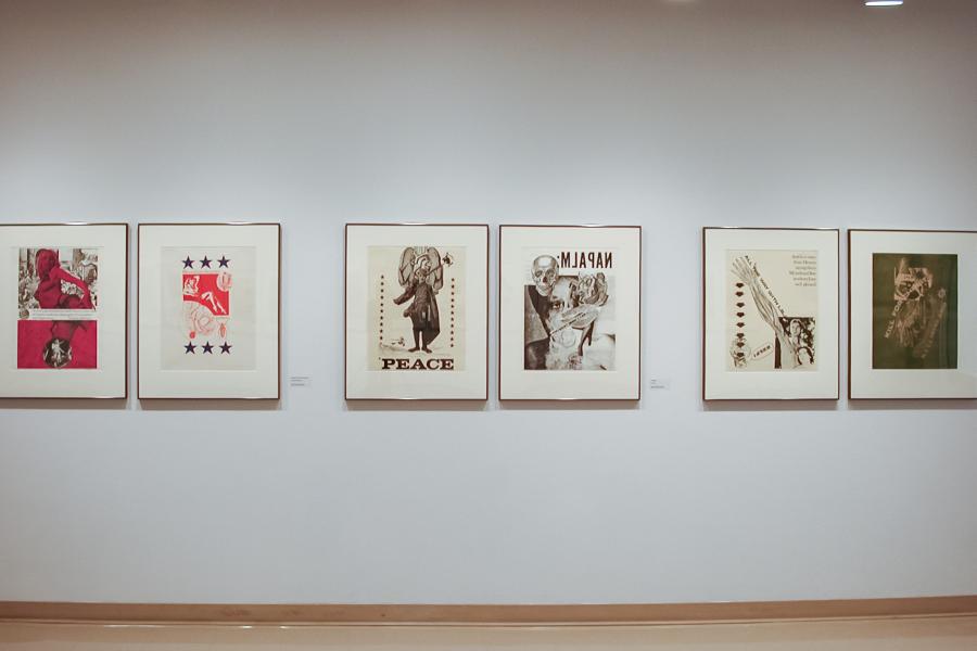 A wall of the gallery, with four diptych graphic collages printed in reds, blacks, and whites and hung in a row, a CRT television showing a protest sign reading “STOP POLICE OBSTRUCTION” on a stand in the wall’s right corner, and a bench in front of it. The furthest right graphic depicts three nude figures in black and white with their hands covering their faces.