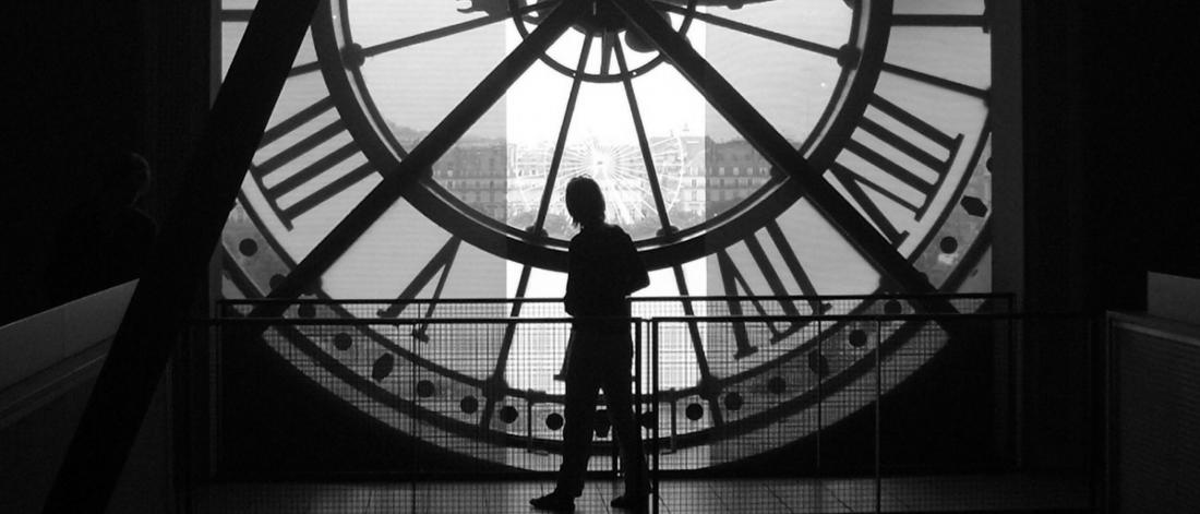A silhouette of a person standing in front of a huge mechanical clock. 