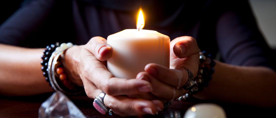 Close up of hands, with many rings, holding a lit candle.