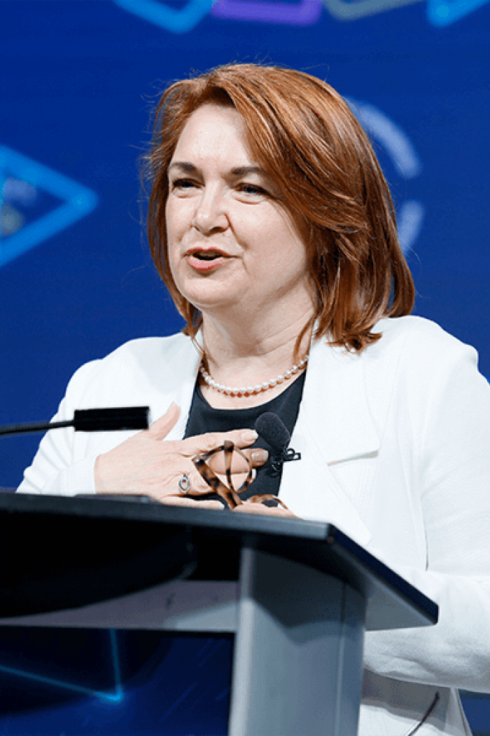 Photo of Labour Studies Alum Bea Bruske speaking at a podium in front of a blue background.