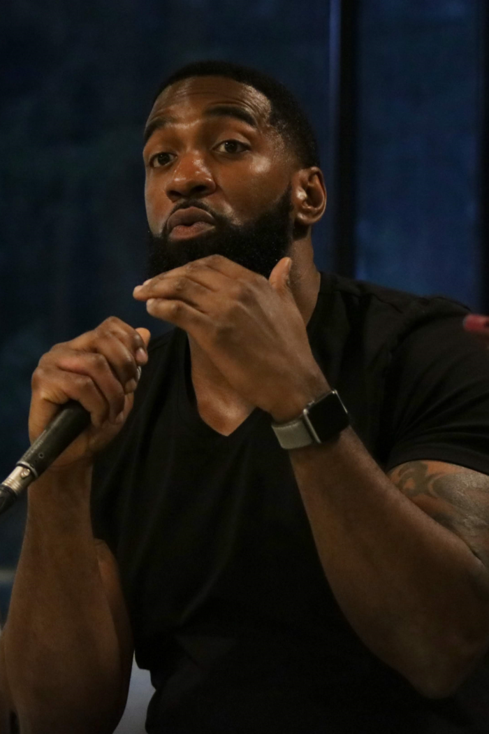 Man speaking into a microphone waving hand animatedly.