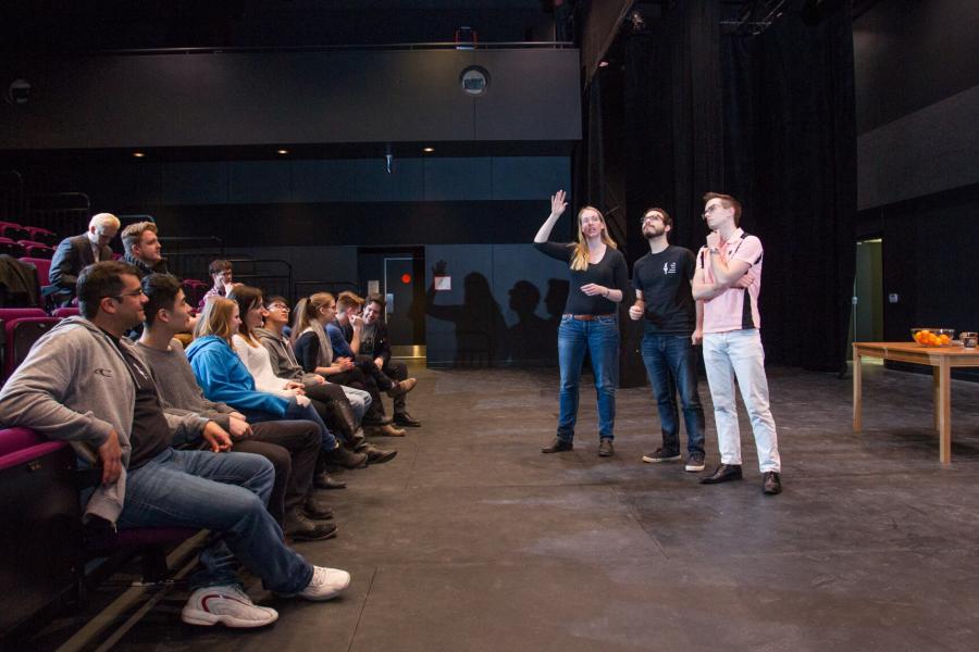 An audience watches as students perform in a theatre.