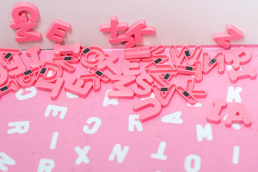 A pink table with white and pink magnetic letters of the alphabet scattered around the surface.