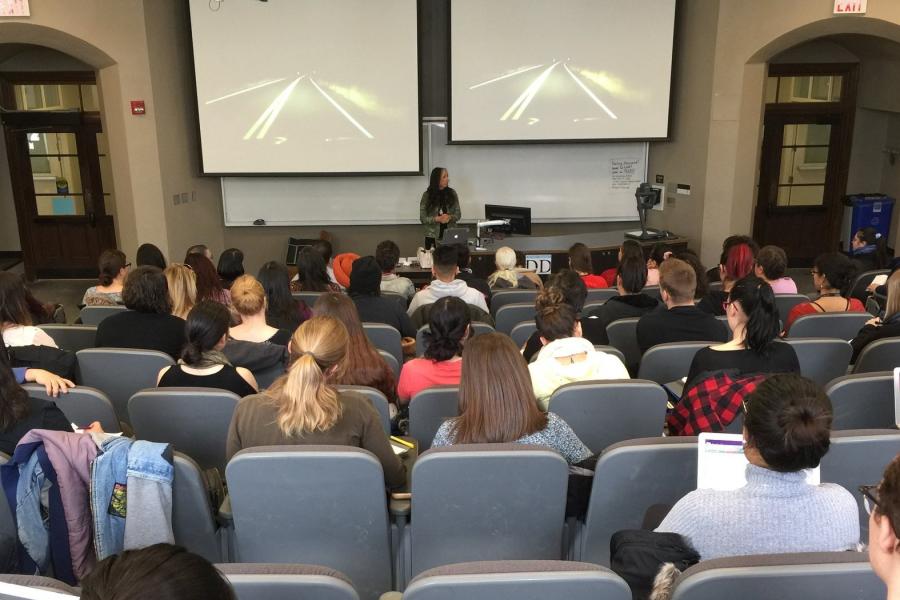 Woman presenting to large class full of students.