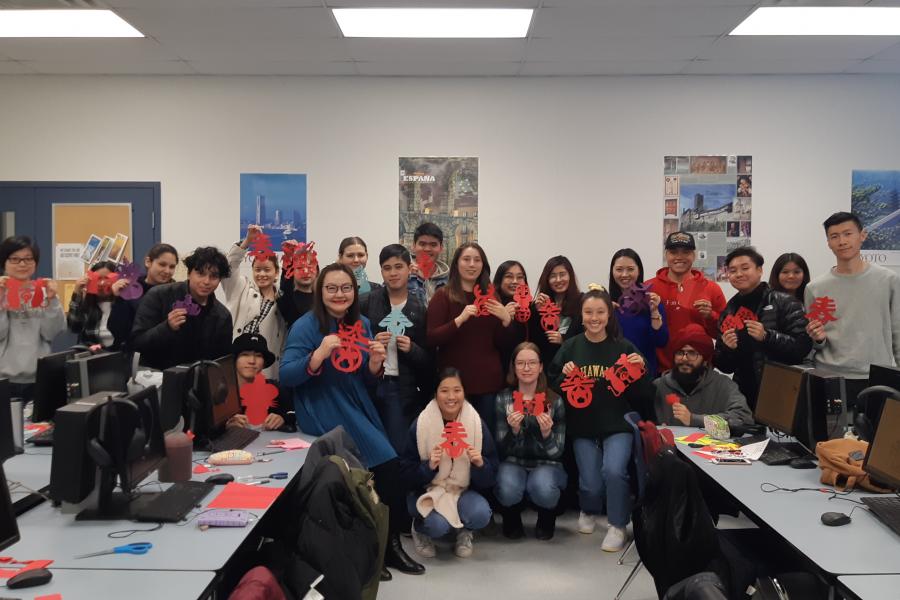 Group of over 15 students holding up paper Chinese calligraphy crafts. 