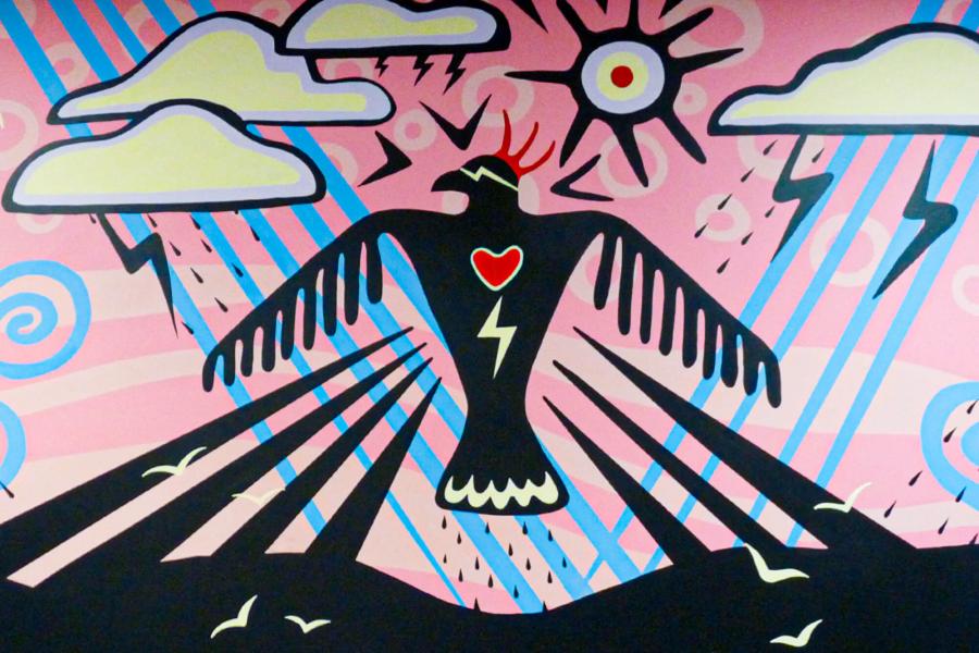 Thunderbird Rising mural. Black bird with red heart on a pink and blue background with clouds and thunderbolts.