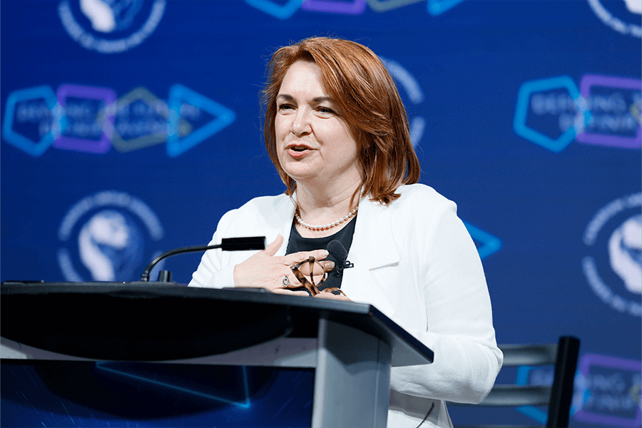 Photo of Labour Studies Alum Bea Bruske speaking at a podium in front of a blue background.