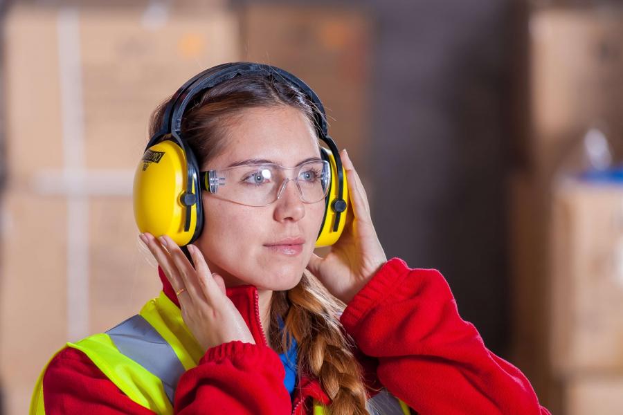 Woman with safety glasses and headset wearing hi-visibility vest.