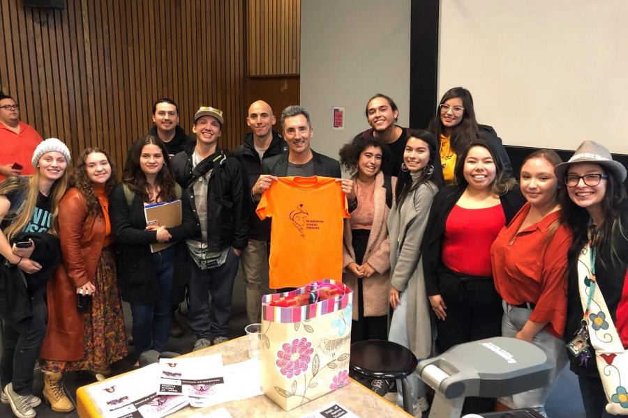 Kent Monkman holding orange T-shirt surrounded by students.