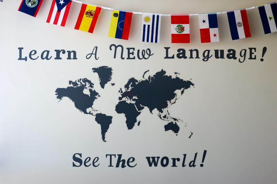 Photo of a banner of flags and a world map on the wall in the Language Centre. Text: Learn a new Language! See the World!