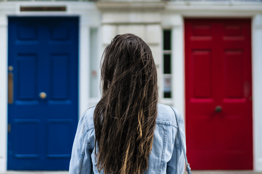 Photo of back of woman facing three doors, one blue, one white, one red.