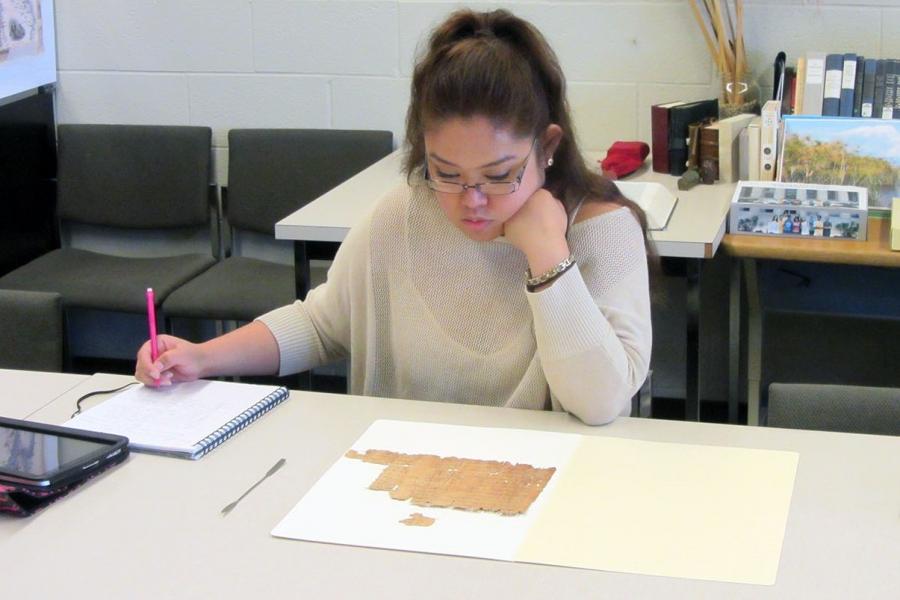 Photo of student studying ancient, fragmented papyrus document.