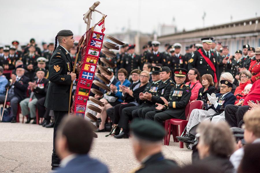 Sergeant Moogly Tetrault-Hamel (left) carries the Canadian Armed Forces Eagle Staff at the Indigenous Sunrise Ceremony in honour of the 75th anniversary of the Dieppe Raid in Dieppe, France on August 18, 2017.