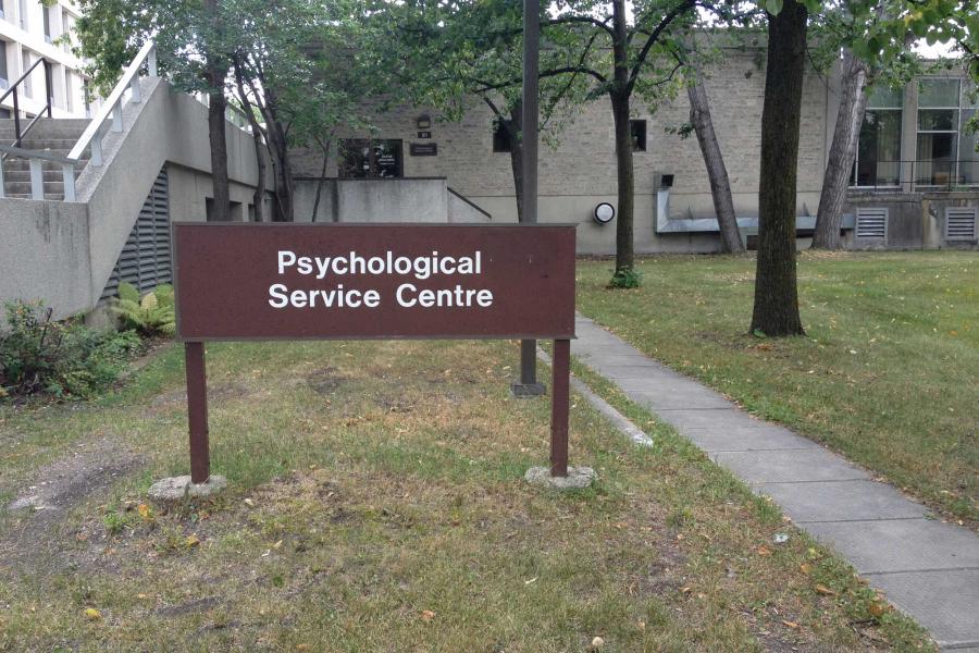 Brown sign to the left of a sidewalk leading up to the Psychological Service Centre. Text: Psychological Service Centre.