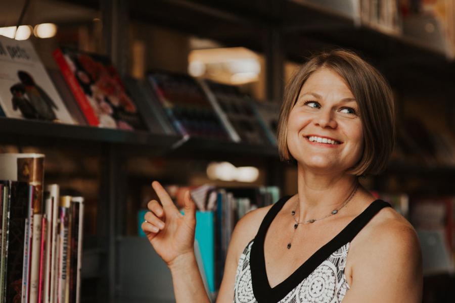 Woman smiling and pointing at shelves of books.