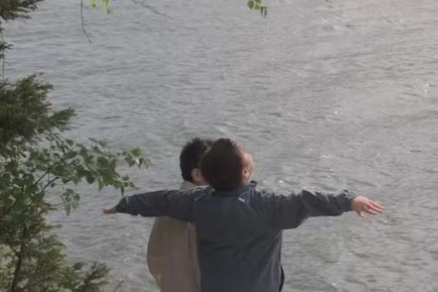 Two boys, arms outstretched, standing alongside a riverbank.
