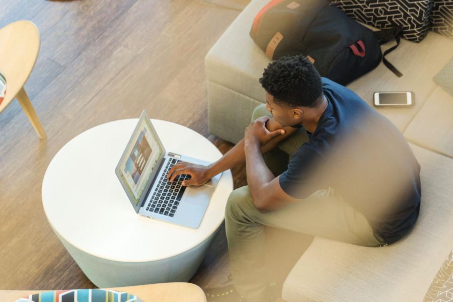 Man in student lounge looking at laptop on table.