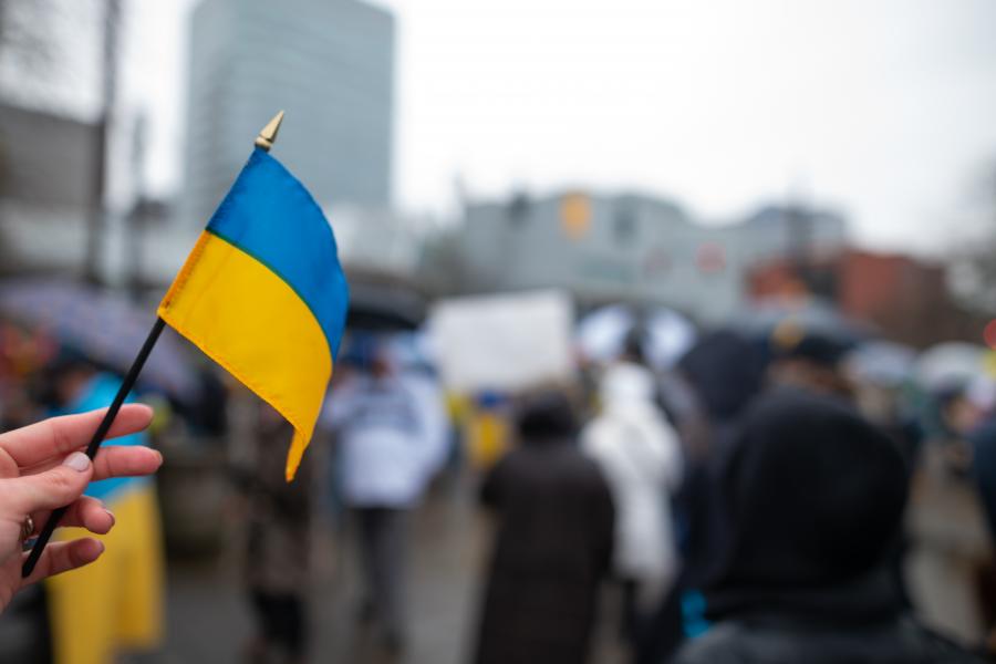 Handheld Ukrainian flag in the foreground, with blurred crowd in the background.