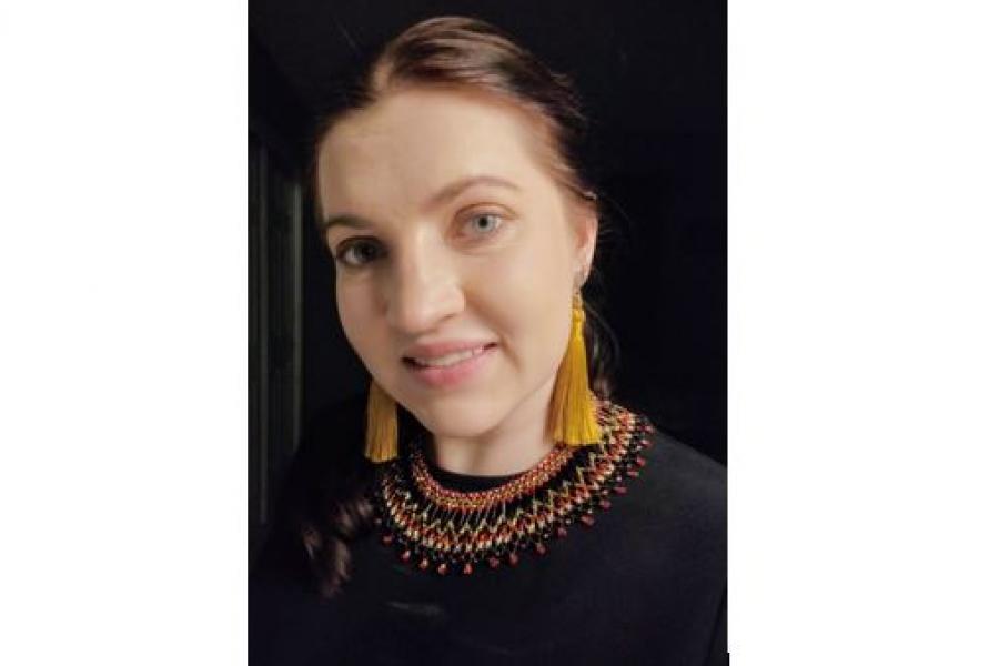 Person wearing long yellow tassel earrings looking into camera against black backdrop.