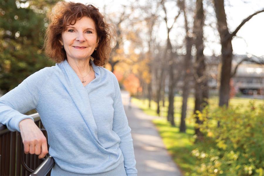 Woman in blue sweater standing in front of a tree lined path.