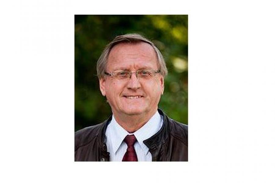 Headshot of man in glasses, shirt and tie, and leather jacket.