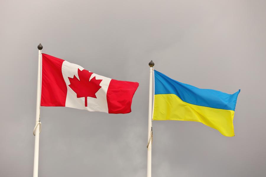 One Canadian flag beside one Ukrainian flag, both on flagpoles.