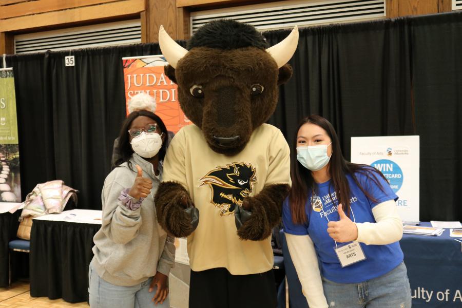 Two students in masks giving thumbs up and standing with Billy the Bison mascot.