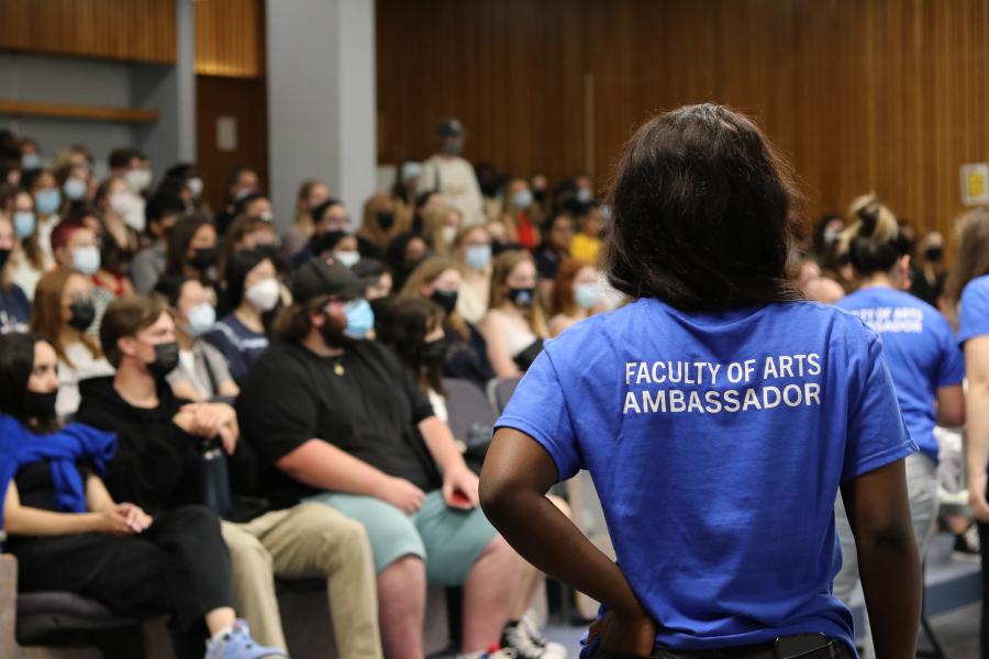 Person with back to camera in foreground, classroom full of students in background.