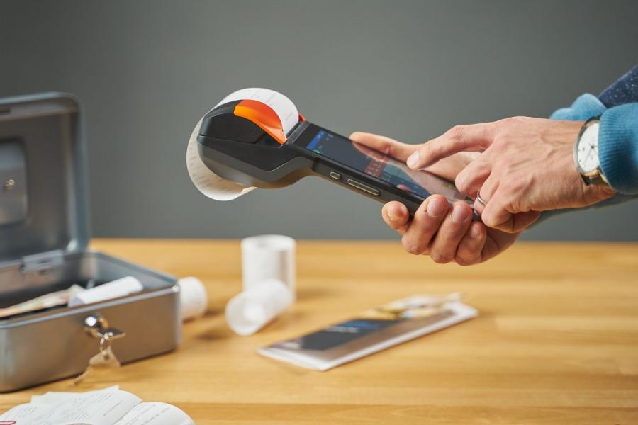 Hands using a mobile payment device with a receipt coming out of the top of the device.