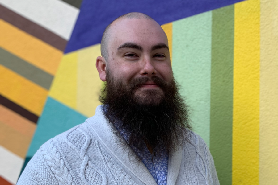 A photo of Nicholas Evans in front of a wall painted with various vibrant colours.