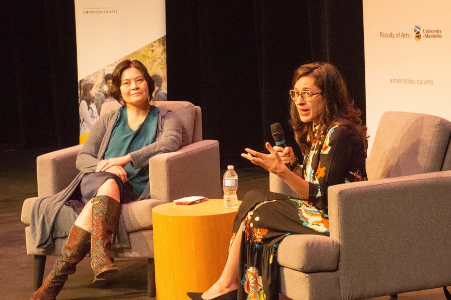 Two individuals in arm chairs on a stage conducting a Q & A with an audience.