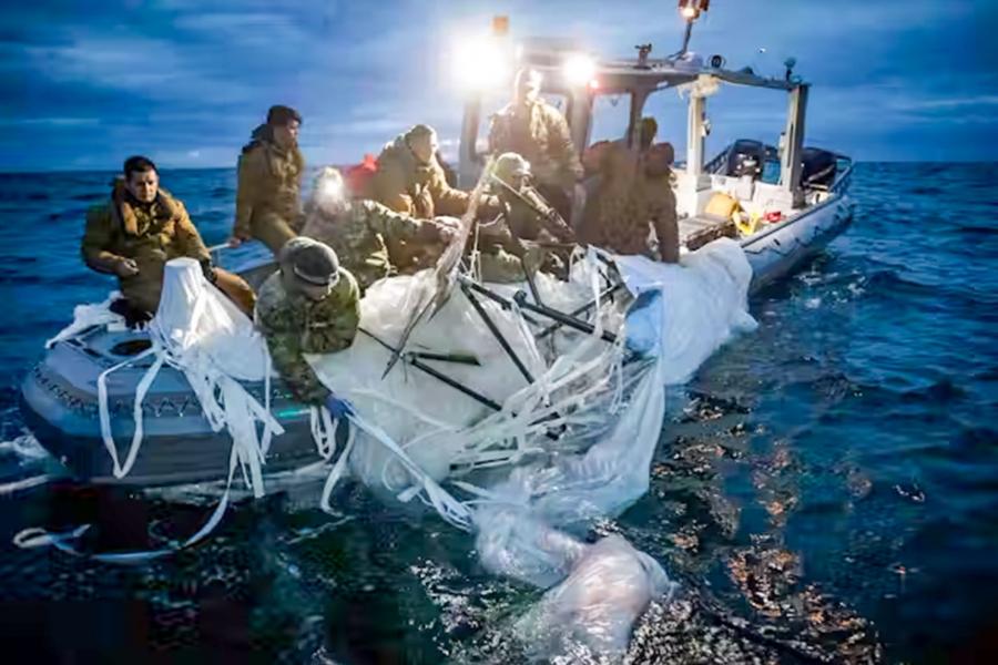 A group of sailors on a boat in the water trying to recover high-altitude surveillance balloon leftover