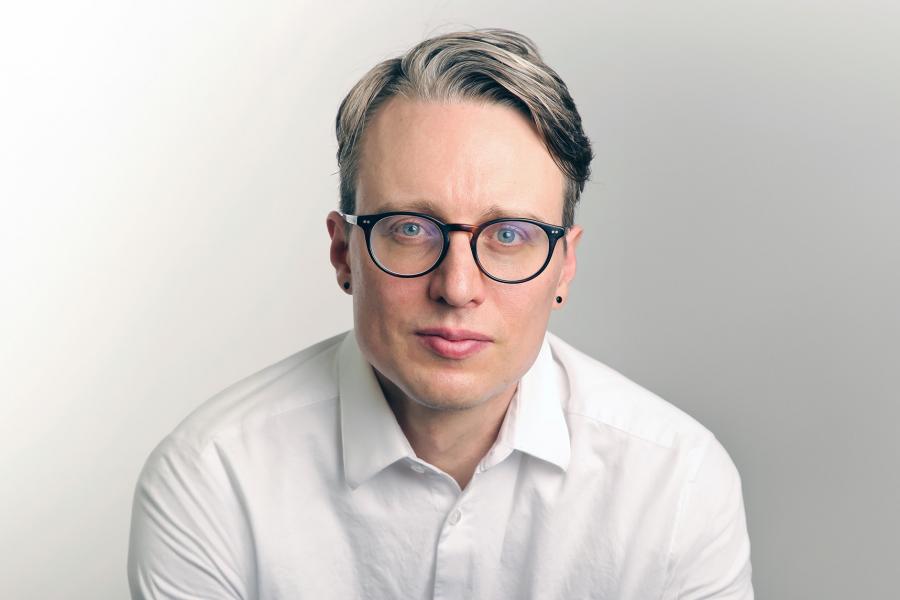 A headshot of Neil McArthur wearing a white shirt with glasses