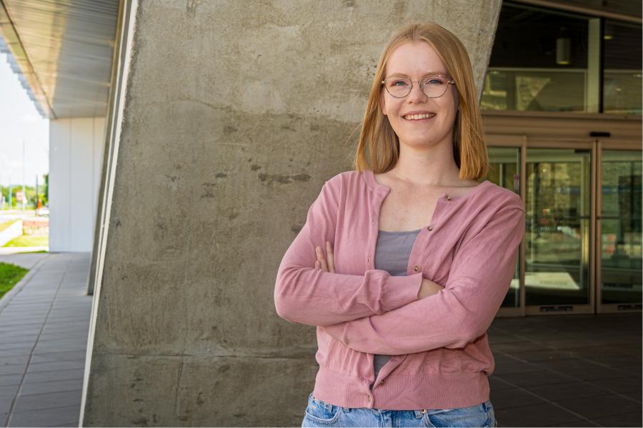 Female wearing glasses, standing with arms crossed in front of a concrete wall.