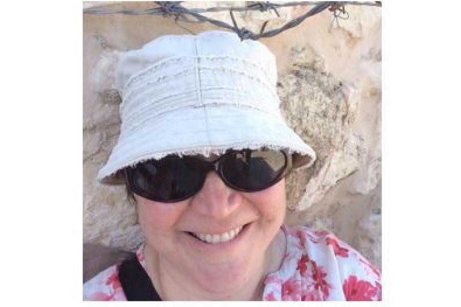Woman wearing a sunhat and dark sunglasses, smiling at the camera.