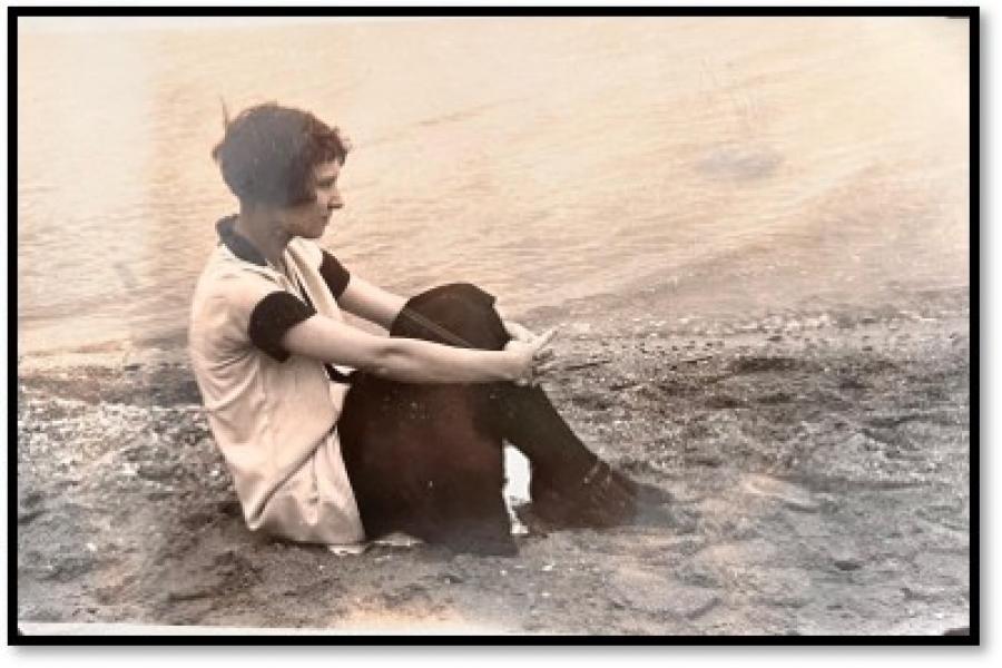Sepia photo of woman sitting on a hilltop with her knees pulled up against her chest.