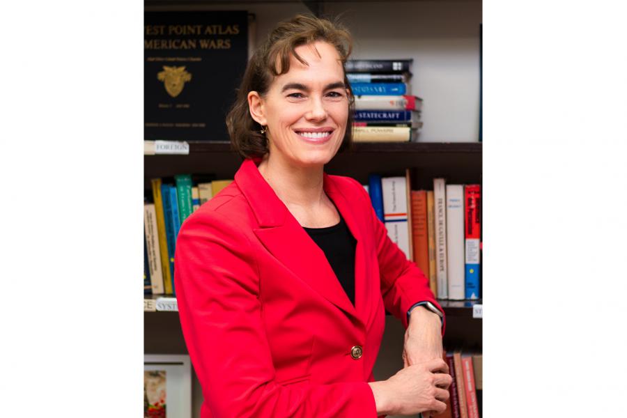 A headshot of Andrea Charron standing in front a bookshelf wearing red jacket