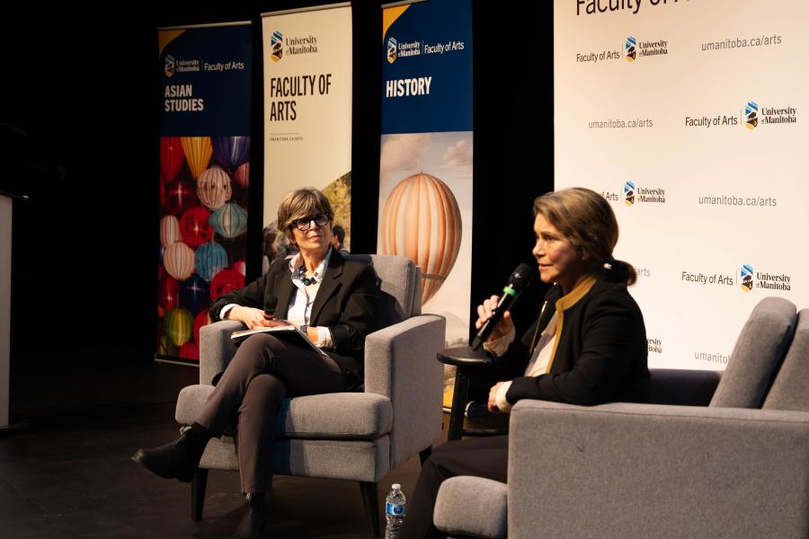 Two women, sitting in armchairs, holding microphones. 