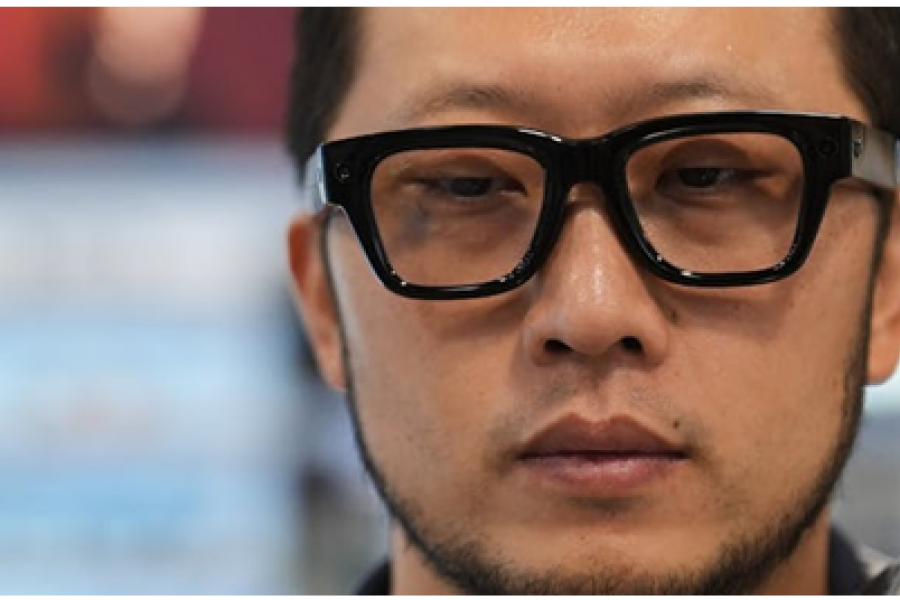 A closeup of a mans face who is wearing black, thick rimmed meta glasses.