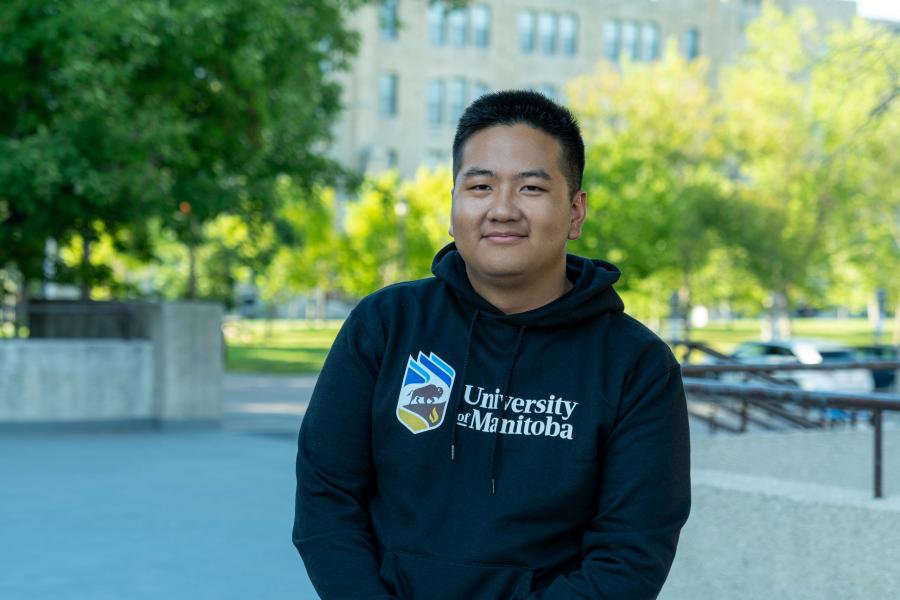 Student wearing a University of Manitoba hoodie standing outdoors on a pathway.