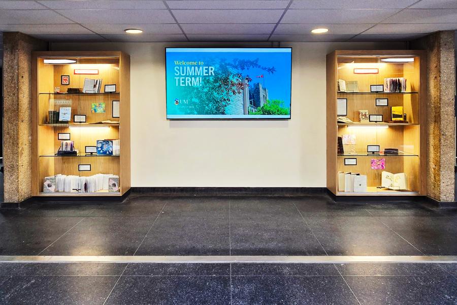Two cabinets with a curated display of student work inside. A large T.V. screen is set on the wall in between the cabinets.
