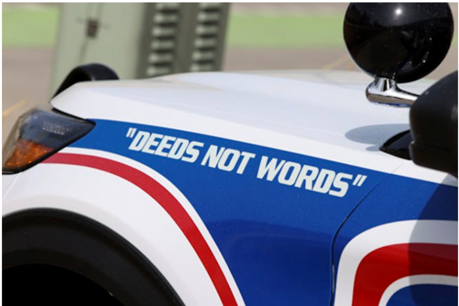 A closeup of a police car hood showing the words deeds not words. 