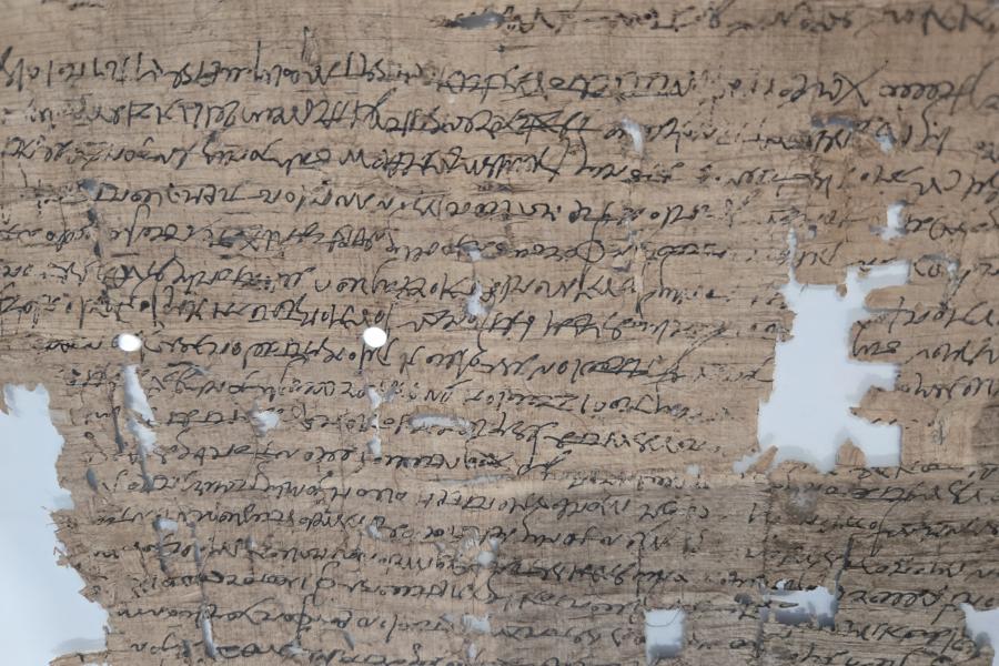 A fragile papyrus document with holes and rips and ancient greek cursive writing on it.